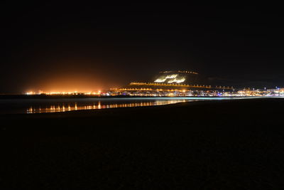 Illuminated city by sea at night