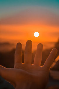 Close-up of hand against orange sky