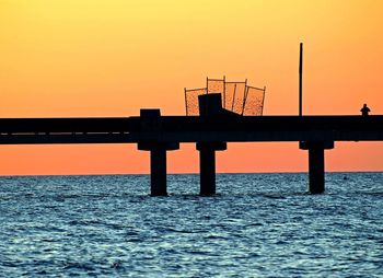 Silhouette bridge over sea against orange sky during sunset