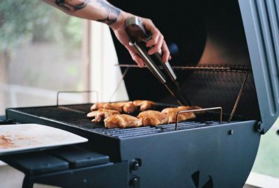 Tattooed hand holding serving tongs with meat on barbecue grill