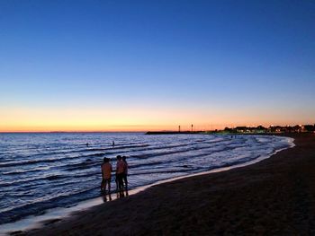 People on beach against sky during sunset