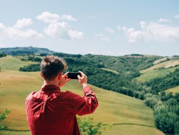 Rear view of man photographing on smart phone against sky