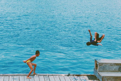 Boy looking at friend jumping in sea