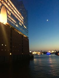 Illuminated buildings by river against sky at night