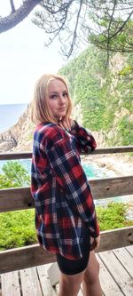 Beautiful woman standing by railing against trees