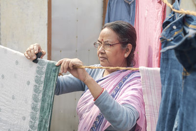 Portrait of a simple looking mature indian woman hanging freshly washed laundry to dry in the sun