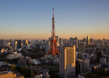 Tokyo tower amidst buildings in city against clear sky during sunset