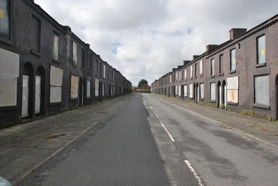 Scenic view of road flaked by buildings against cloudy sky