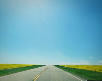 Empty road amidst land against blue sky