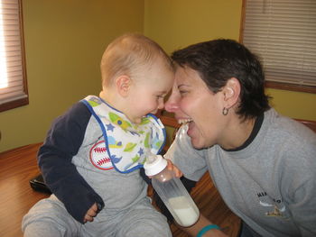 Mother playing with son holding milk bottle at kitchen counter