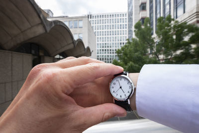 Midsection of man holding clock against built structure