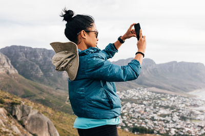 Side view of young man photographing while standing on mountain