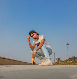 Full length of man crouching on road against clear blue sky
