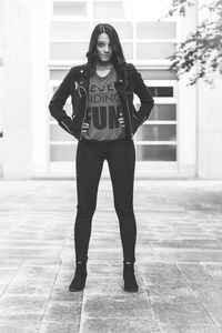 Full length portrait of young woman with hands on hip standing against building