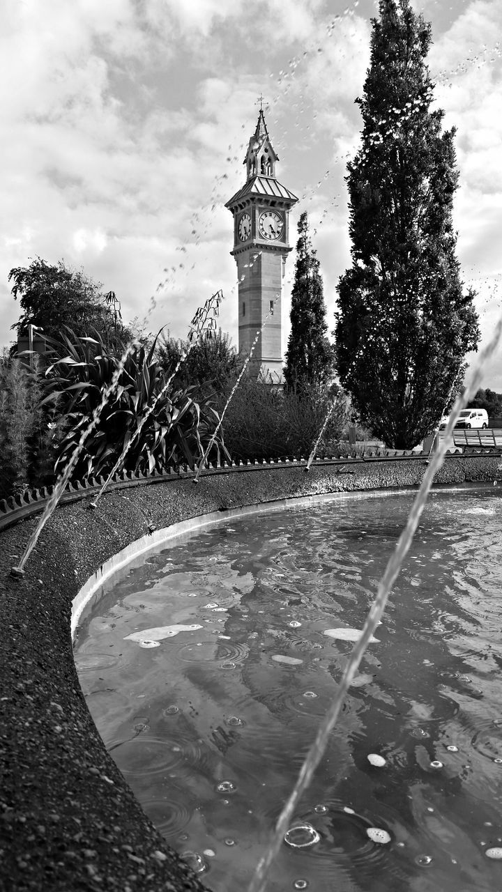 tree, water, building exterior, architecture, sky, built structure, transportation, street, road, fountain, motion, puddle, cloud - sky, day, outdoors, travel destinations, mode of transport, reflection, travel, nature