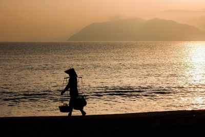 Silhouette of woman walking on beach against sky during sunset