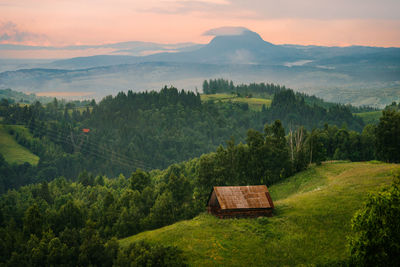 Barn on hill against mountain at sunset