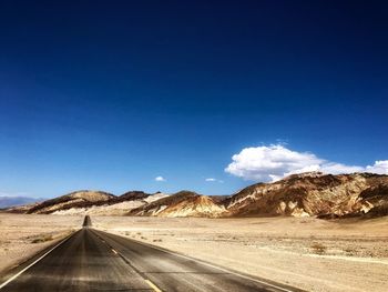 Road amidst desert against blue sky