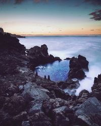 Rocks on beach against sky during sunset