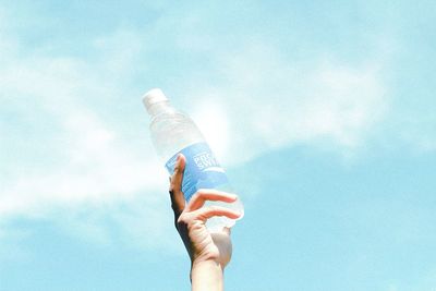 Low angle view of person holding bottle against blue sky