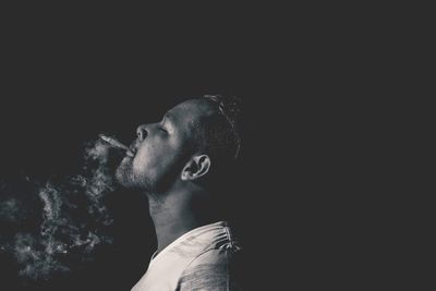 Side view of man smoking cigarette against black background