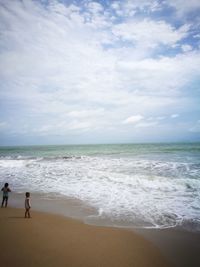 Boys standing on sea shore against sky