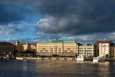 Buildings by river against cloudy sky