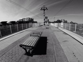 Empty bench on elevated walkway in city against sky