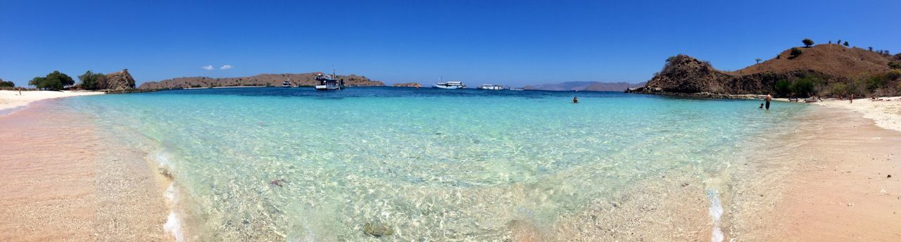 beach, sea, water, sand, clear sky, blue, shore, tranquil scene, beauty in nature, scenics, tranquility, copy space, mountain, nature, coastline, incidental people, surf, wave, horizon over water, sunlight