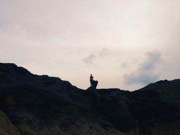 Low angle view of woman standing on rock formations against sky