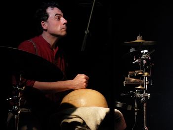 Young man playing drum set against black background