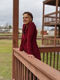 Side view of a smiling young woman sitting on railing