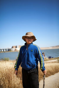 Portrait of young man standing on field against clear blue sky