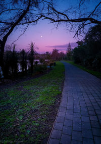 Footpath amidst grass against sky at sunset