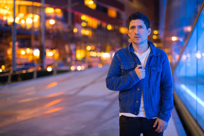 Portrait of young man standing on illuminated street at night