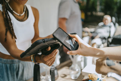 Hand of woman doing contactless payment while shopping at flea market