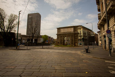 Road by buildings in city against sky