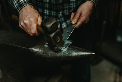 Midsection of man hammering latch in workshop