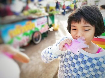 Cute girl eating cotton candy while standing outdoors