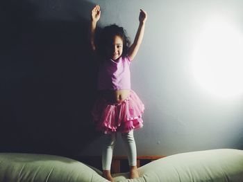 Portrait of happy ballerina standing on bed with arms raised