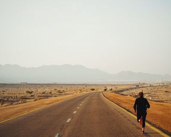 Rear view of man walking on road against clear sky