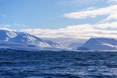 Scenic view of sea and snowcapped mountains against sky