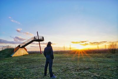 Rear view of man standing on field against sky during sunset