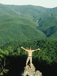 Rear view of shirtless man standing on rock with arms out