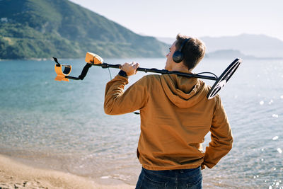 Rear view of man with arms outstretched standing at beach