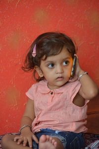 Portrait of cute girl sitting against red wall