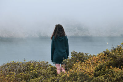 Rear view of woman standing by plants against sky