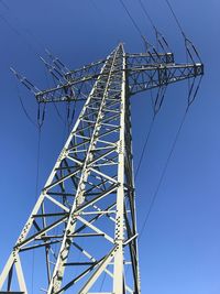 Low angle view of electricity pylon against blue sky