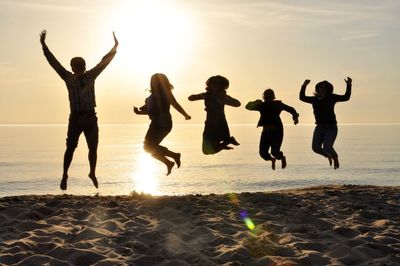 Friends jumping at beach against sky