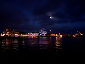 Illuminated city by sea against sky at night